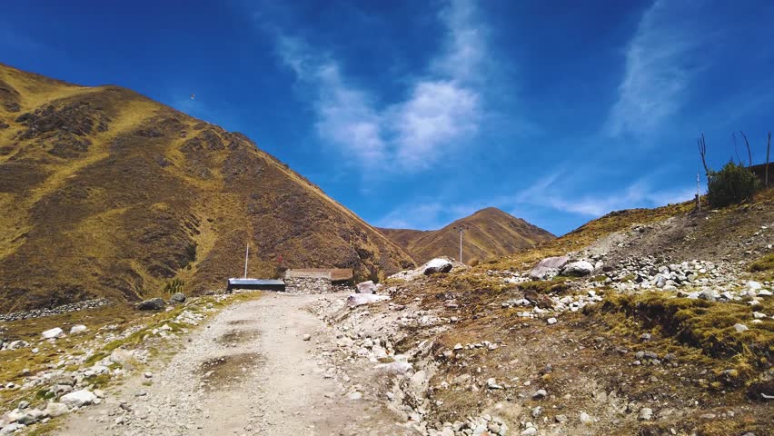 Mountain road leading to stone houses in rural Chaullacocha, surrounded by dry hills under blue sky. Driver POV shot
