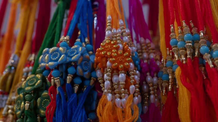 flower shaped Rakhi bracelets made with beads and colorful threads, tied in a bunch and hanging for sale during Raksha bandhan festival, with soft flickering ceiling lights, parallax shot, 4k, 25p
