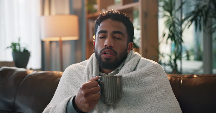 Sick man, blanket and cold with tea on sofa for influenza, virus or flu symptoms in home. Male person, viral infection or shiver with cup, mug or herbal drink for warmth, illness or fever in house