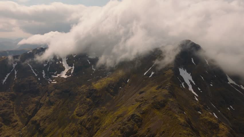 Aerial drone footage of Bidean Nam Bian, the highest mountain in Glencoe, Scotland, covered in snow. Sweeping views of snowy peaks, deep valleys, and dramatic Highland scenery