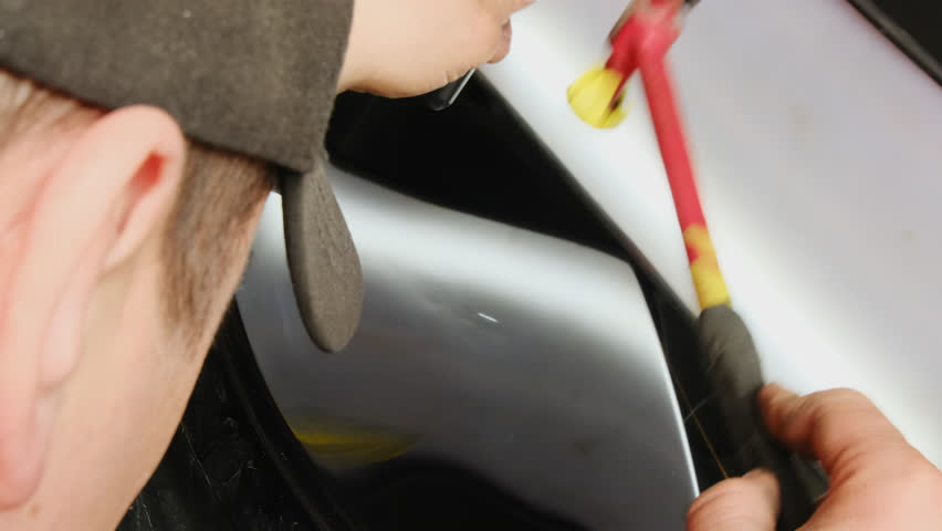 Master taps surface of slide with hammer affecting car surface. Man watches process of removing unevenness performing task in workshop