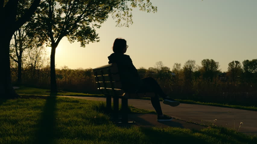 A silhouette of a woman sits on a bench and rests, sunset time. Rest time
