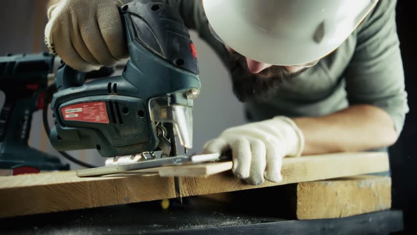 Carpenter Using Jigsaw To Cut Wood Plank.Professional Woodworking Craft. Home Improvement Project. Industrial Power Tool.Manual Labor, Workshop Environment. Construction Worker Safety Carpentry Skills