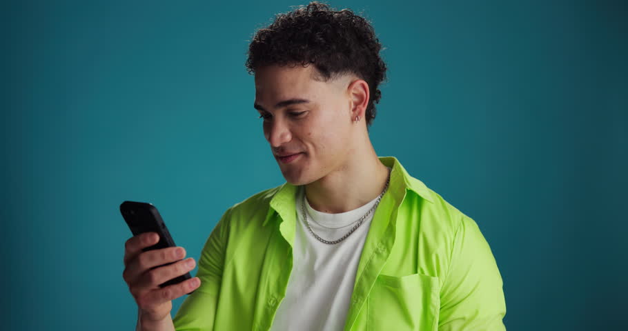 Happy, man and surprise with phone in studio for good news, lottery winner or online announcement. Excited, person and celebration with smartphone on blue background for giveaway or competition promo