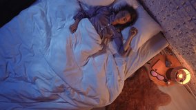 Frustrated young woman in pajamas lying awake in bed at night, holding up an alarm clock with a tired expression. Top view of scene illustrates the struggle of insomnia and sleeplessness. - Powered by Shutterstock - Get 15% off with code: PIKWIZARD15