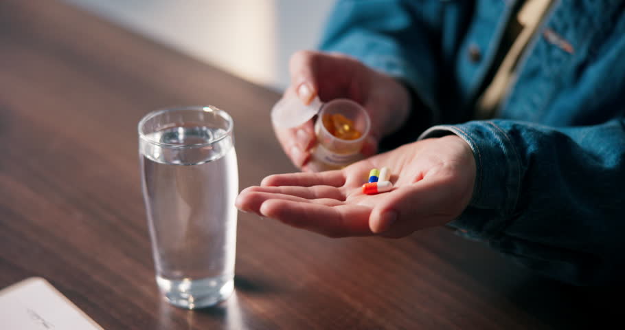 Pills, above and hands of woman in home with medicine, prescription and medication for recovery. Health, water and person with container for vitamins, supplements and drugs for medical symptoms