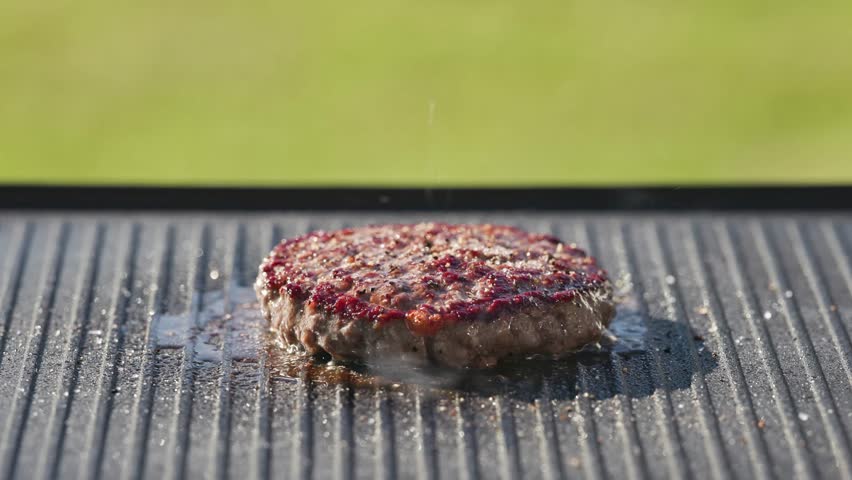 cook put melted cheese slice on freshly grilled hot burger patty meat on grill pan surface, food closeup, outdoor cooking