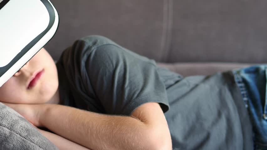 An alpha generation child sleeps on the couch with virtual reality glasses. Relaxing with gadgets. Modern digital life. Children born in the digital world. Sleeping in virtual reality. sstkTechnology.