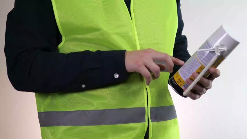 A builder or handyman holds a can of foam in his hands, reads its description and properties. Familiarization with the instructions for using foam materials.