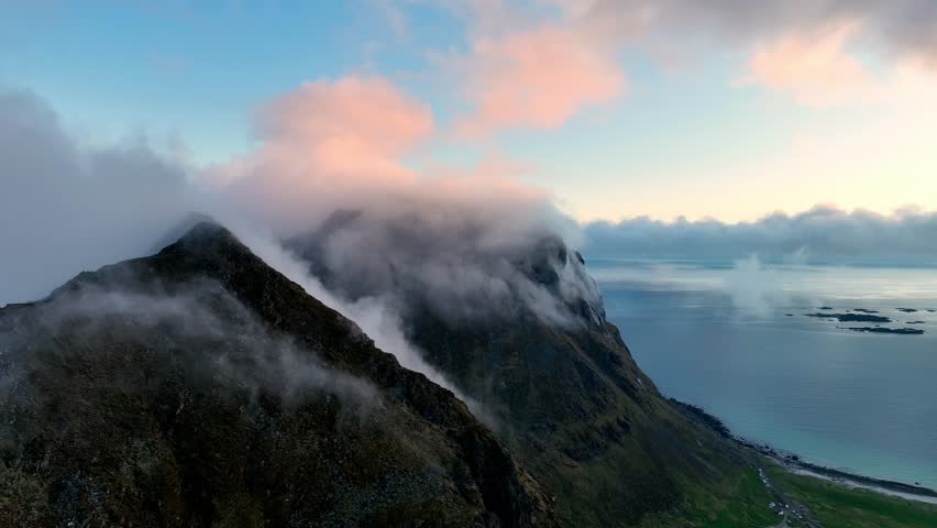 Fog wraps Mannen peaks as ocean fog climbs over mountains and Utakleiv glows in pink midnight sun in Lofoten