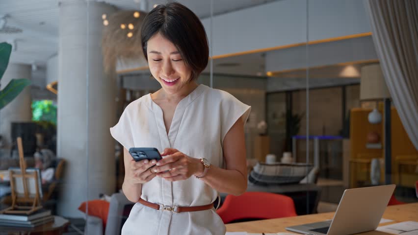 40s mature Asian business woman manager ceo using cellphone mobile phone trade app. Smiling mature female businesswoman holding smartphone in office for trading, work chatting, looking at screen - Powered by Shutterstock - Get 15% off with code: PIKWIZARD15
