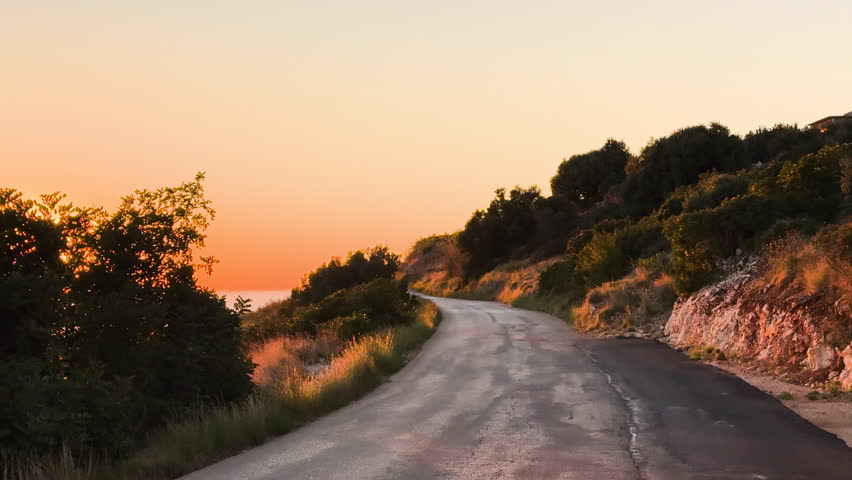 LENS FLARE: Travel along a winding road through lush Mediterranean countryside with views of a breathtaking golden sunset over the glistening Adriatic Sea. Dramatic and picturesque end to the day.