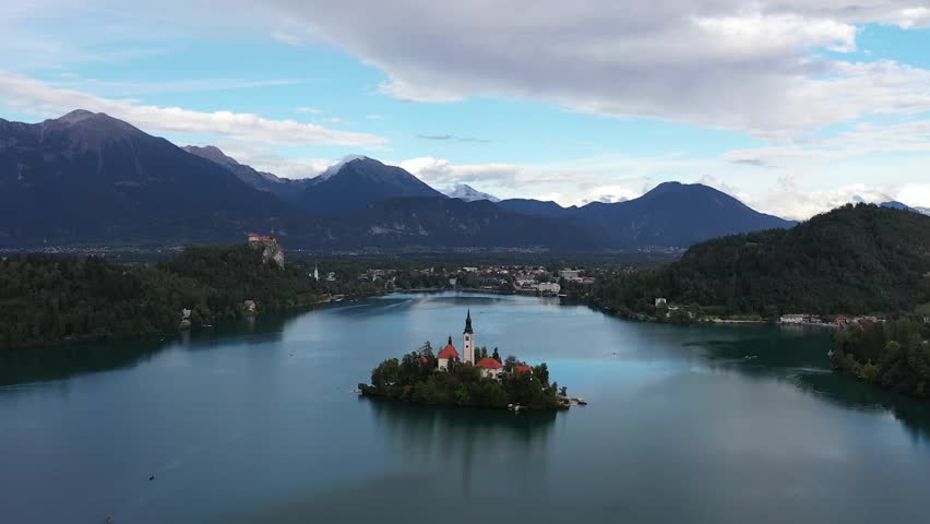A drone orbits the fairytale island of Lake Bled, circling the church at its heart while alpine mountains rise majestically beyond, shimmering water and lush greenery completing Slovenia’s