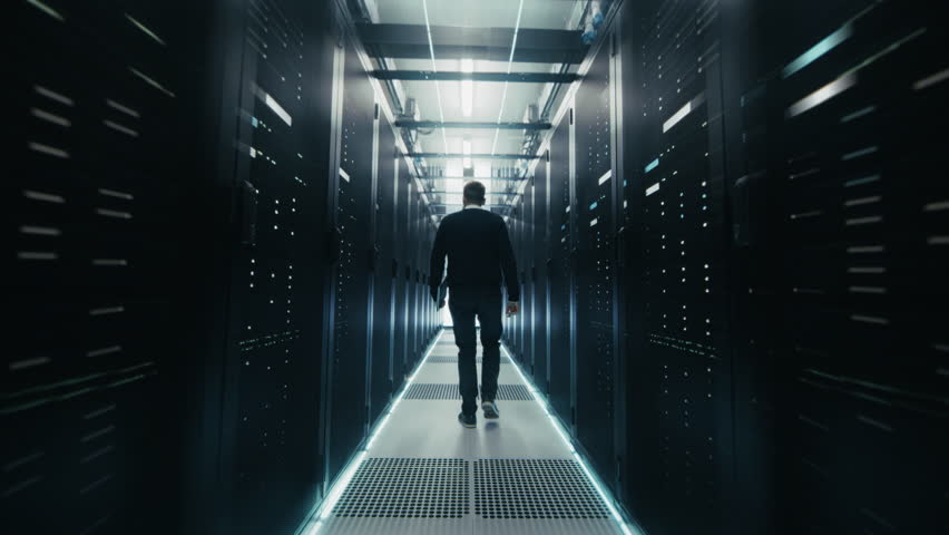 Following Shot: Engineer Walks Between Rows of Server Racks in Data Center. Advanced Network Hardware Cloud Computing, Artificial Intelligence, and Cyber Secure Business Operations.