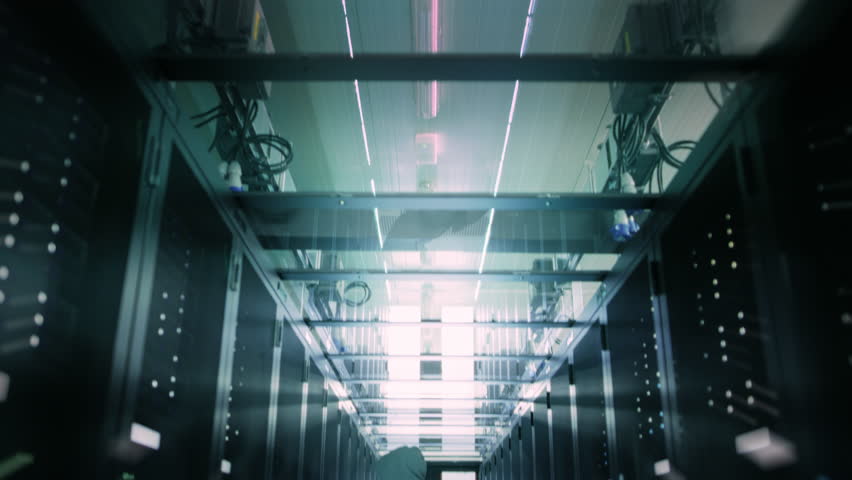 Hacker in a Hoodie Stands in a Data Center Aisle, Using a Laptop to Execute a Virus Cyber Attack. Server Room Hacking, Cyber Security Threats, and Vulnerabilities Within Modern Server Room - Powered by Shutterstock - Get 15% off with code: PIKWIZARD15