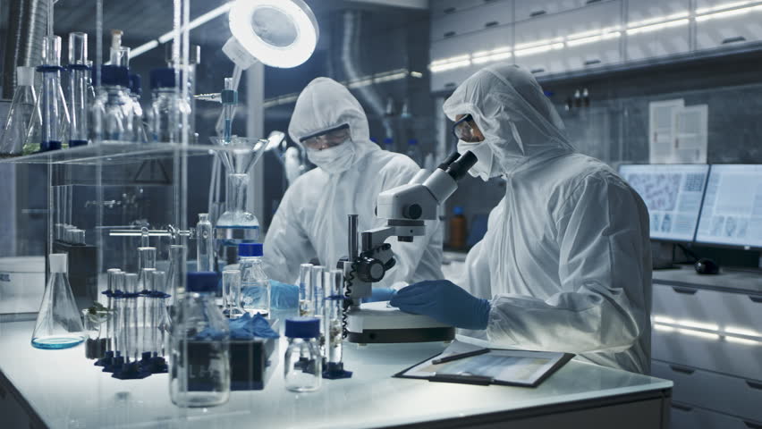 Two Scientist in Full Protective Suit Works in Sterile Lab, Examining Biological Samples with Microscope. Modern Research, Biomedical Analysis and Healthcare Innovation and Pharmaceutical Development