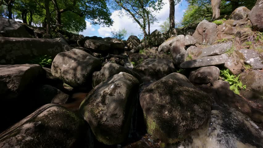 A close-up view of Burbage Brook in Padley Gorge, Derbyshire, with foamy water falling over tufted rocks