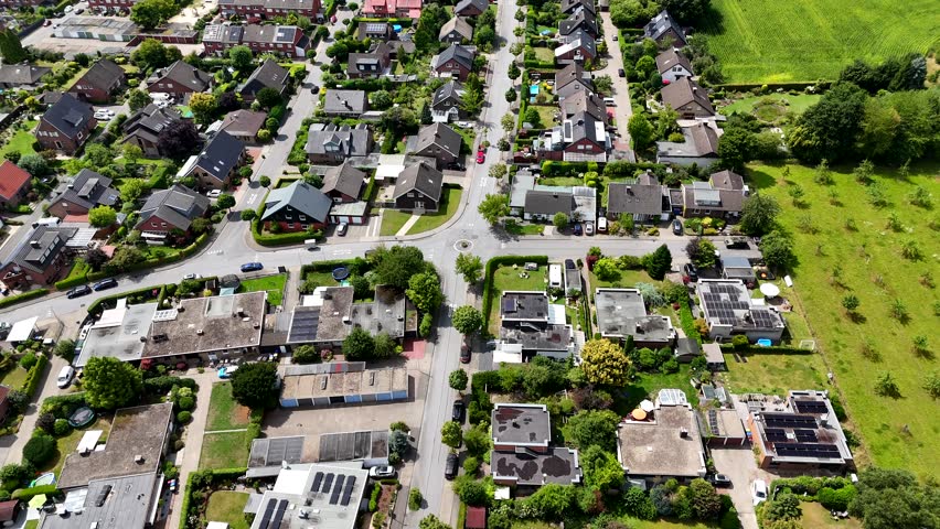Single family houses with solar panels on roof in quiet suburb district of town. Rural fields border. Aerial top down flyover. Row of homes and townhouses in subdivision residential area.