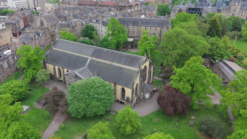 Cinematic drone orbit of Greyfriars Kirkyard, Edinburgh’s historic cemetery. Atmospheric aerial view of gothic tombstones, old church, and surrounding stone walls.