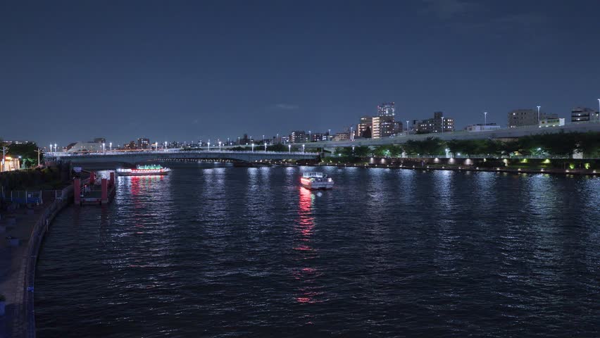 Multiple illuminated boats cruise along Tokyo's vibrant Sumida River at night, creating a bustling scene with city lights reflecting on the water.