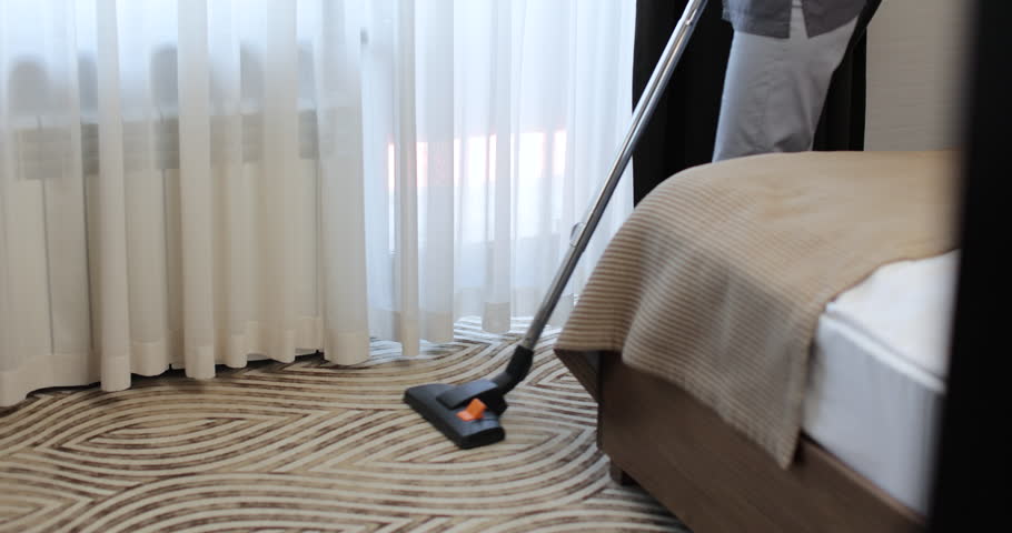 Close up woman vacuums a carpet in a hotel room. The concept of service and cleaning in the hotel room. Hotel service.
