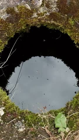 Stone falling into a round hole in the ground into water. Waves on the water after a disturbance. Slow motion cinematic close up shot. A hole in the ground in an ancient temple to store various things
