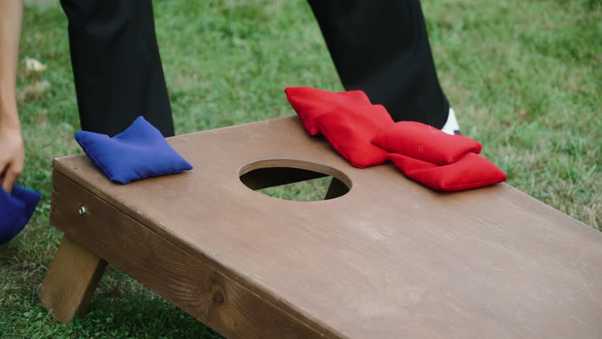 Cornhole assistant helps stack bags on wooden board during practice. Improving skills in popular, active american game. Abstract impersonal shot with unrecognizable people.