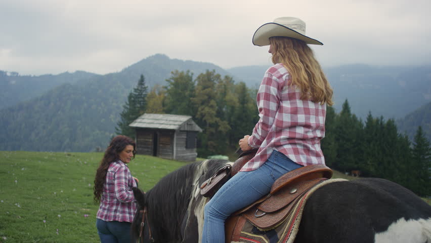 Girl on a horse ride adventure in misty mountains, horseback lesson in scenic nature setting at riding school with experienced cowgirl instructor, rear view.