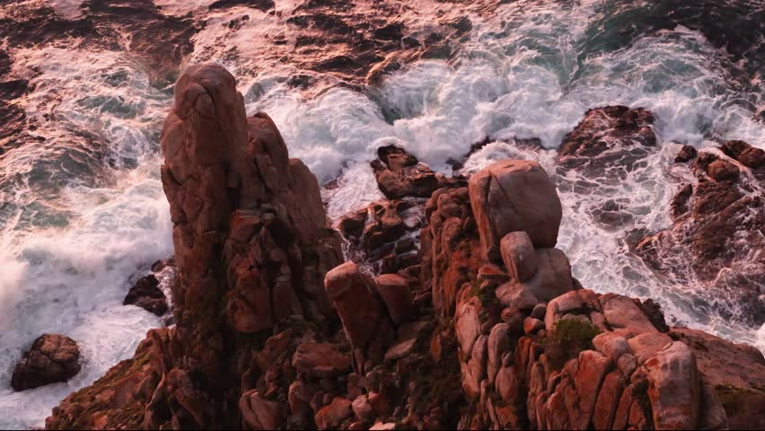 A slow-motion of foamy ocean waves hitting the rocks of cliffs by the shore at dusk in South Africa