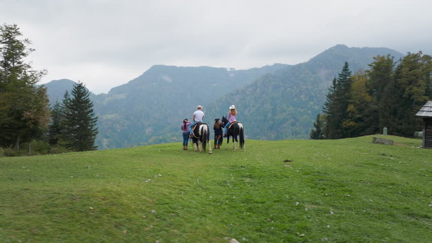 Cowboy and cowgirl on horseback enjoying a scenic mountain view during a weekend getaway at a Western-style ranch riding school, on a cloudy morning, aerial shot.