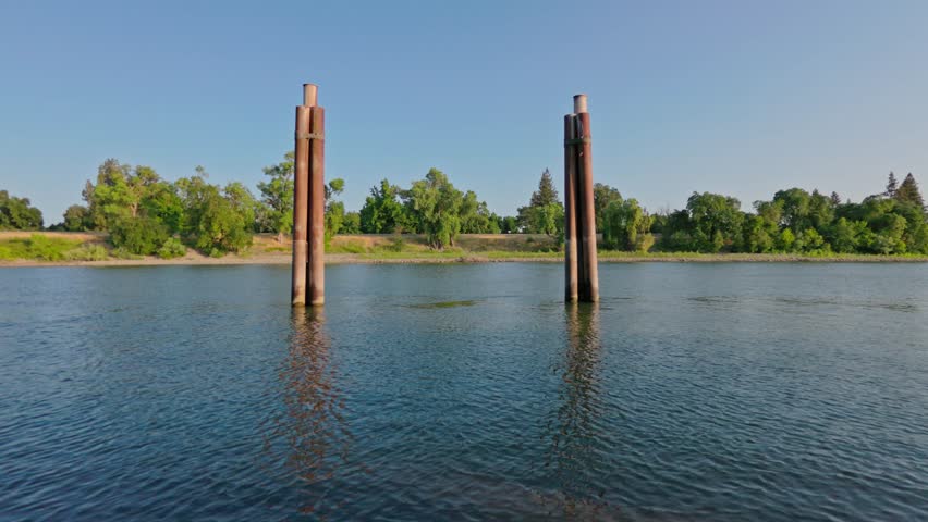 A time lapse of calm river water flowing past two pillars with trees lining the distant shore