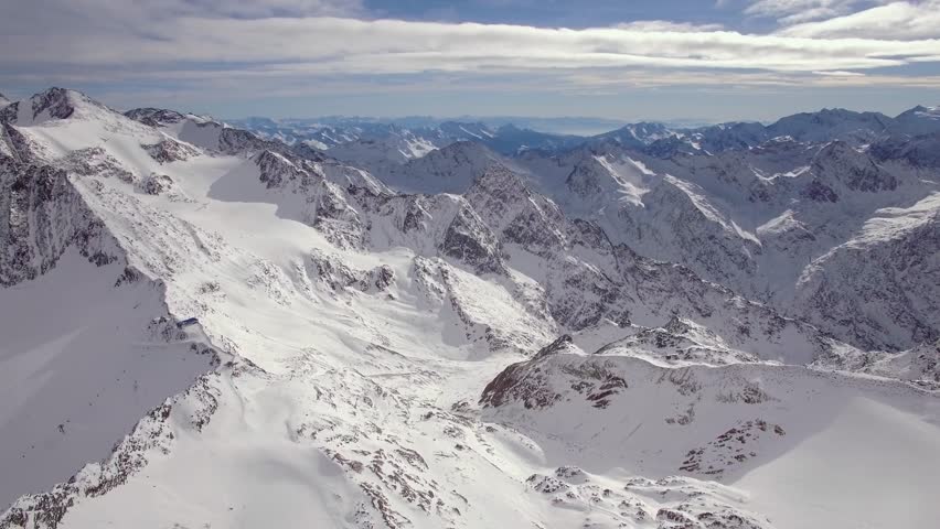 An aerial Snow-covered alpine mountain range with sharp peaks and vast icy slopes under a partly cloudy sky, Austria
