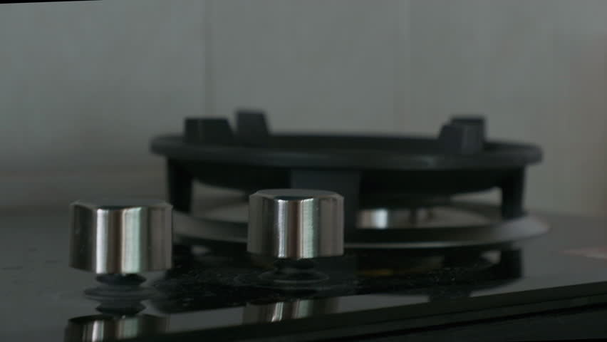 Gas stove burner with blue flame cooking on kitchen countertop and hand adjusting knob flame