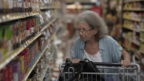 An elderly senior woman navigates a busy grocery store aisle, carefully examining the shelves stocked with various food items as she pushes her shopping cart. - Powered by Shutterstock - Get 15% off with code: PIKWIZARD15