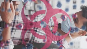 Animation of virus cells and biohazard sign over caucasian man wearing face mask. global covid 19 pandemic and health concept digitally generated video. - Powered by Shutterstock - Get 15% off with code: PIKWIZARD15