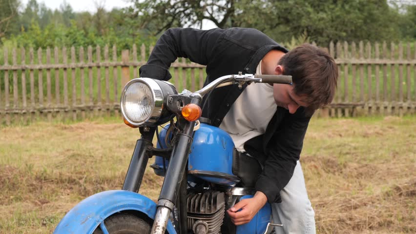 Young man fixing his vintage motorcycle in countryside