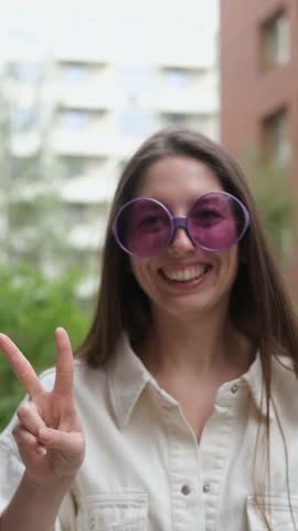 Cute cheerful charming girl poses for camera in summer on city street, hands and fingers showing V sign
