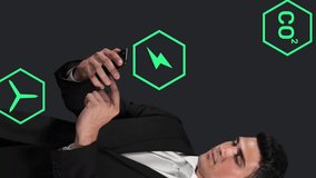 Animation of digital icons over caucasian businessman using smartphone against grey background. Eco-friendly sustainable energy and business technology concept - Powered by Shutterstock - Get 15% off with code: PIKWIZARD15