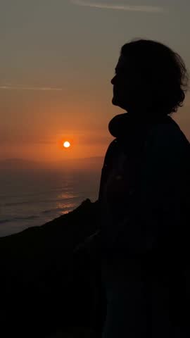 Silhouette portrait of a woman tourist texting on her phone during sunset, surrounded by warm light and peaceful atmosphere.