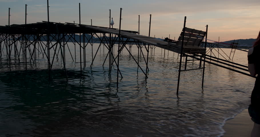 Sunset tranquility at a rustic pier nestled along the shoreline with gentle waves lapping against wooden supports