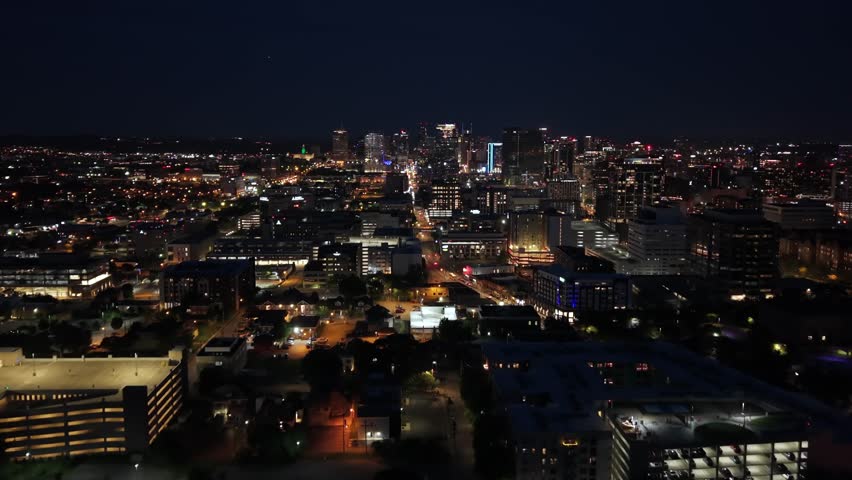 Establishing shot of Nashville, Tennessee skyline at night with glowing lights of a bustling metropolis - forward aerial view