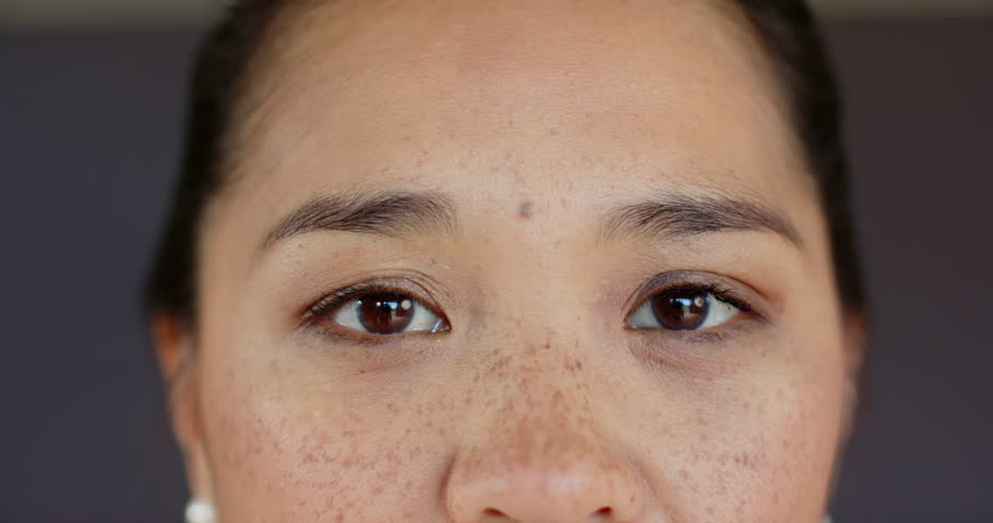 At photographer cue, Asian woman wearing pearl studs in studio blinking, shifting gaze for portrait. Portrait, beauty, elegance, minimalism, sophistication, introspection, lighting