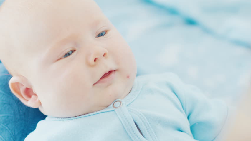 Mother plays with her newborn son with deep blue eyes in a bright room