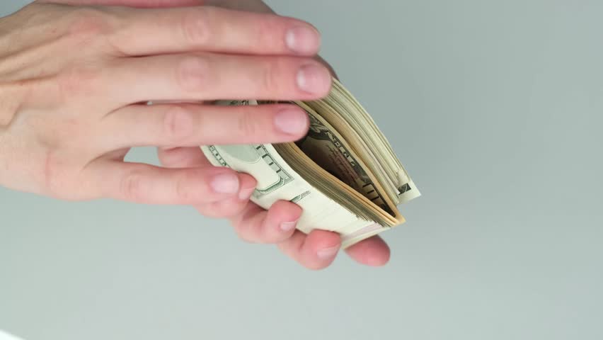 A hand holding a wallet with a lot of money in it. The wallet is open and the money is visible