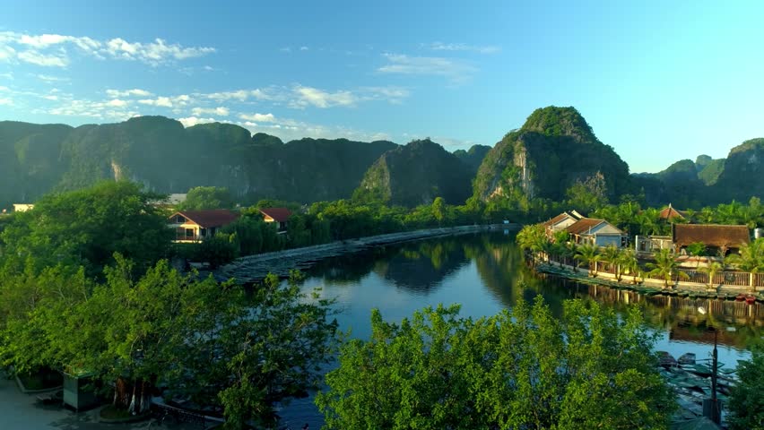 Scenic 4K Aerial View of Tam Coc, Ninh Binh, Vietnam. Stunning Natural Landscape with River, Limestone Mountains, Traditional Village Architecture under a Bright Blue Sky. Tropical trees, houses homes