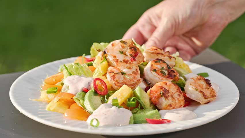 Chef put grilled shrimps on portion of freshly prepared healthy vegetable salad  on plate. outdoor cooking, food close-up
