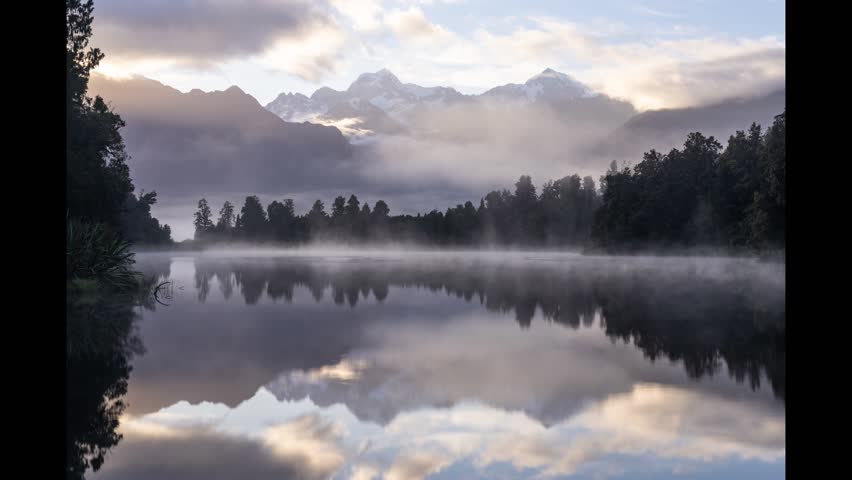 Time-lapse of sunrise at Lake Matheson, New Zealand, showing the calm water perfectly reflecting Mount Cook and Mount Tasman.
