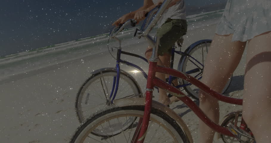 couple pedaling beach cruisers along shoreline, chatting and pointing toward ocean in travel ad. Romantic, leisure, adventure, vintage, scenic, relaxation, summertime