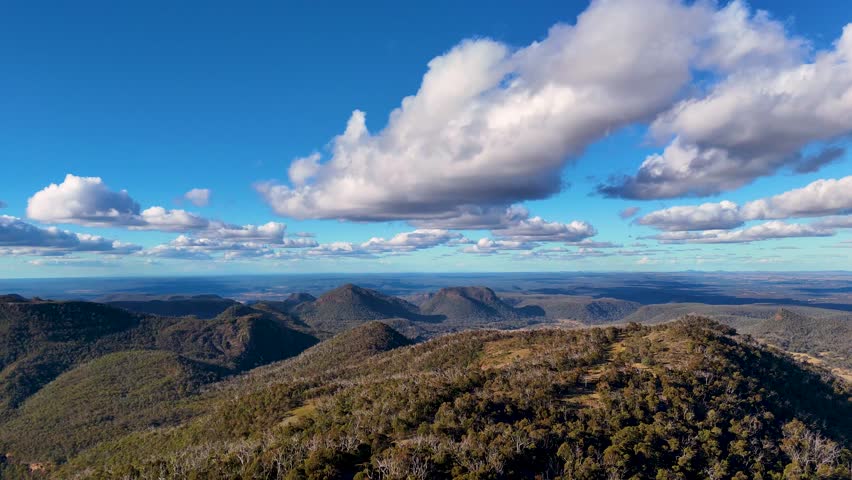 Drone captures sweeping aerial views of Warrumbungle National Parkâs rugged mountain landscape, gum forests, and dramatic clouds in golden late afternoon sunlight