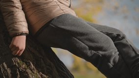 closeup view of child legs and hand resting on tree trunk in tranquil autumn setting, soft sunlight highlights cozy clothing and textured bark while fall colors blur in peaceful background - Powered by Shutterstock - Get 15% off with code: PIKWIZARD15
